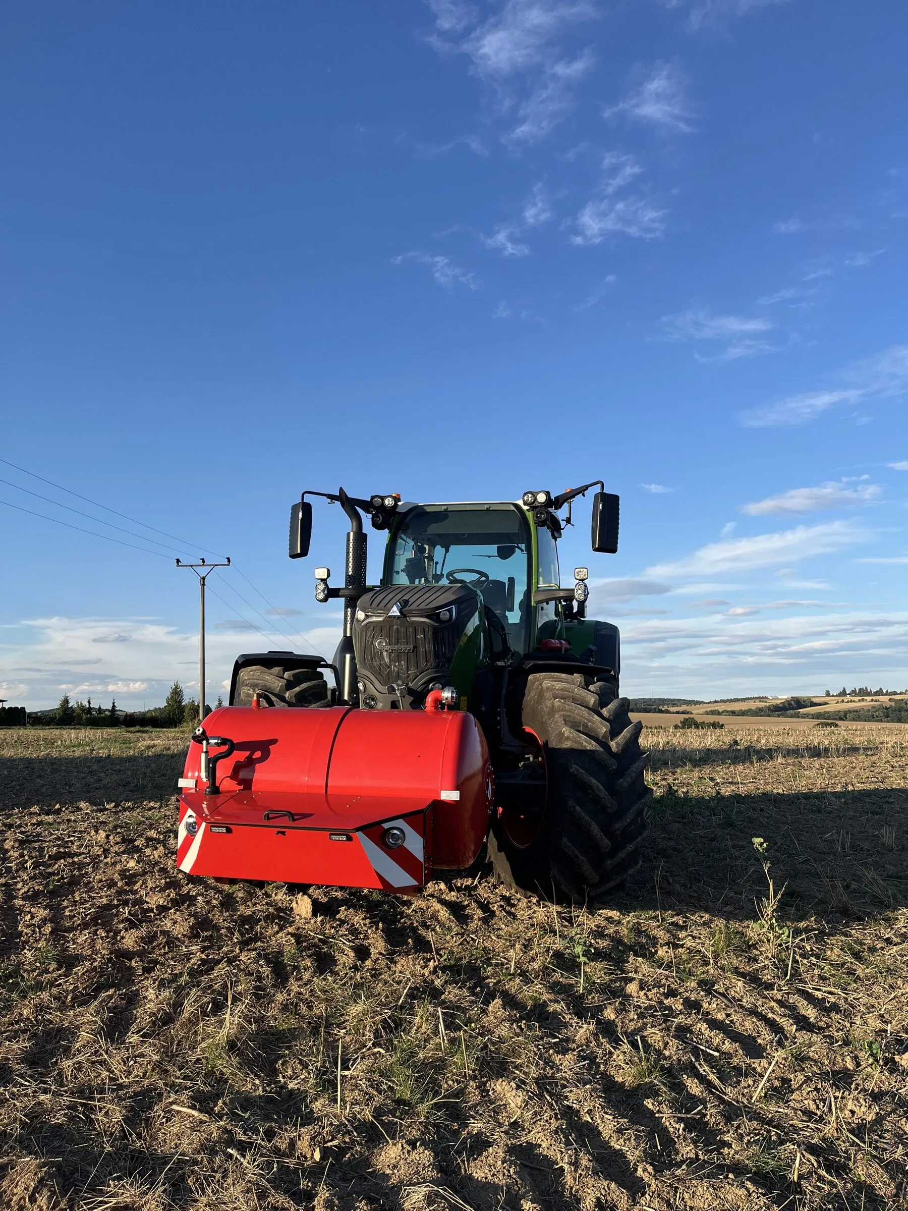 Traktor Fendt s nádrží HYDROTANK na čelním tříbodovém závěsu na zoraném poli pod modrou oblohou